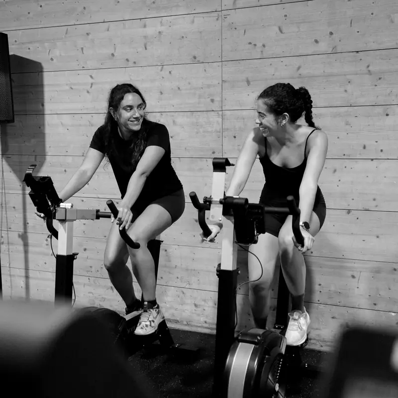 Dos atletas pedalean en bicis de aire y se ríen