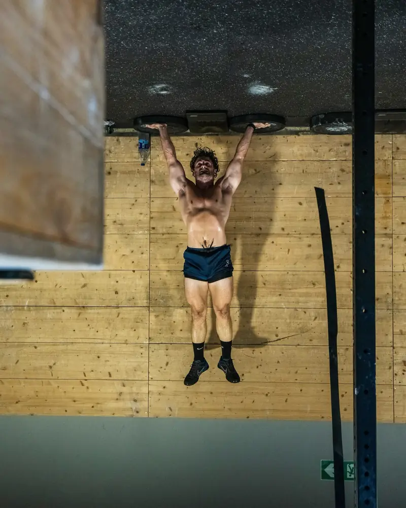 Atleta colgado de la barra frente a la pared de madera